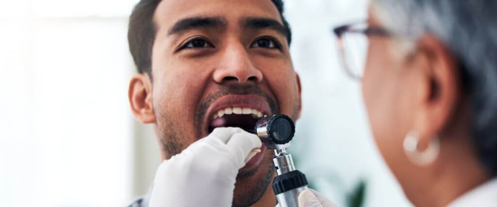 Dentist performing oral cancer screening on a male patient