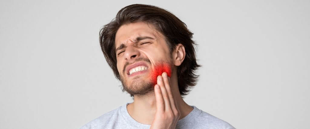 Young man with a toothache and tooth infection holding his jaw in pain