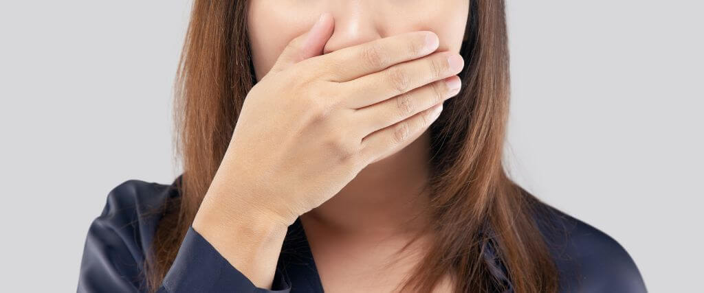Woman covering her mouth due to bad breath, halitosis